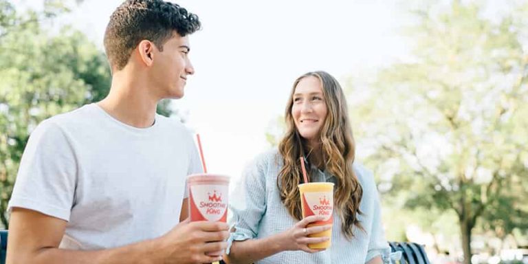 A man and a woman sitting on a bench with drinks in their hands.