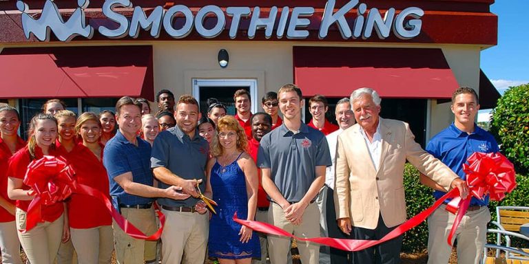 A group of people ranked No. 14 on Entrepreneur's Franchise 500 cutting a ribbon in front of a Smoothie King.