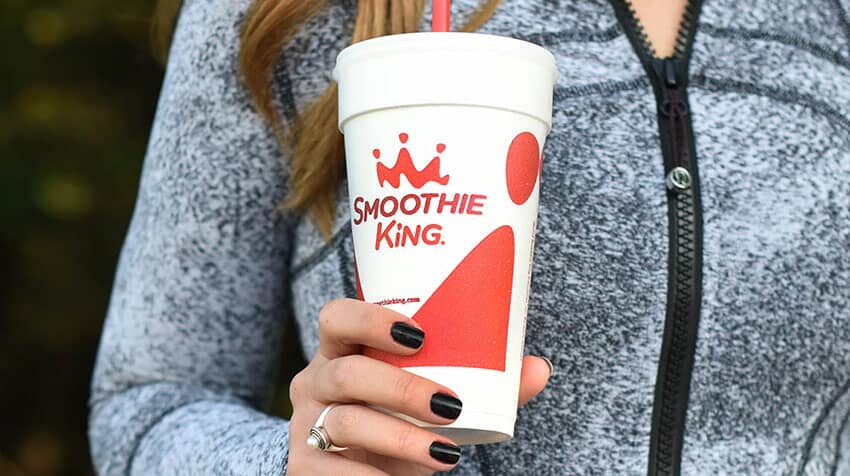 A woman holding a cup with a Smoothie King logo, showcasing the evolution of the smoothie industry.