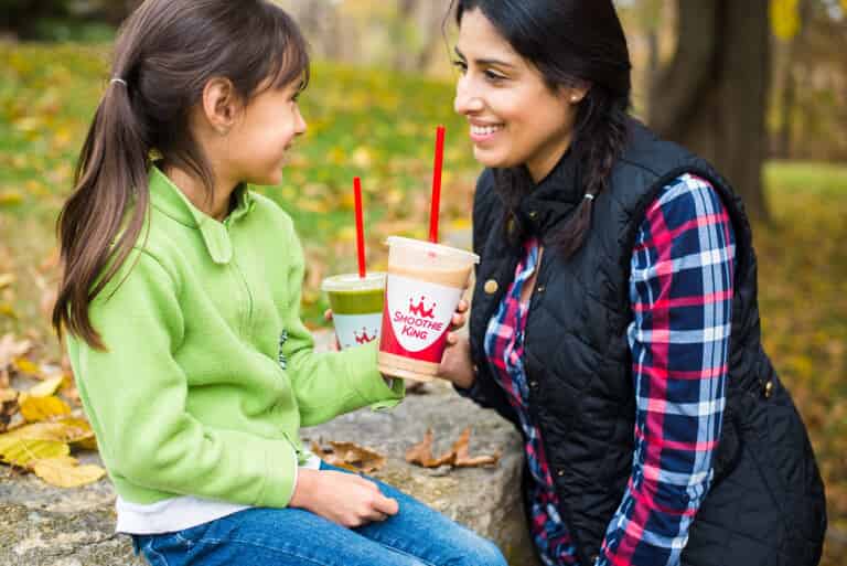 A mother and daughter experiencing the evolution of the smoothie industry while sitting on a rock and drinking a smoothie.