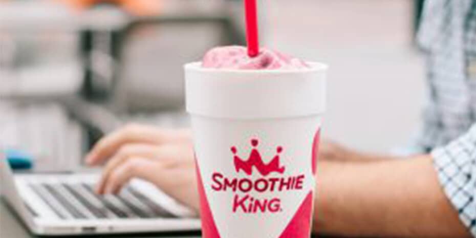 A man is utilizing catering to promote his Smoothie King cups at a table.