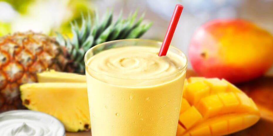 A tropical smoothie with mangoes and pineapples on a wooden table.