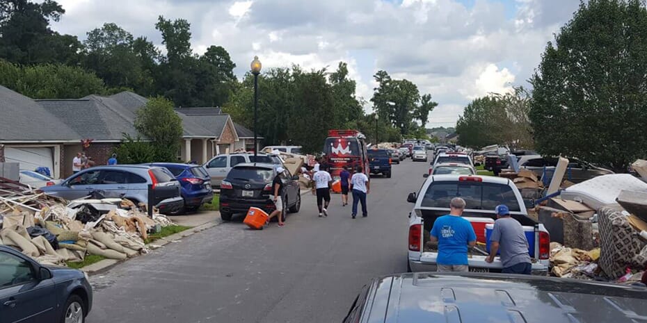 Franchisees prioritize flood-torn communities over own needs, standing amidst debris on a street.