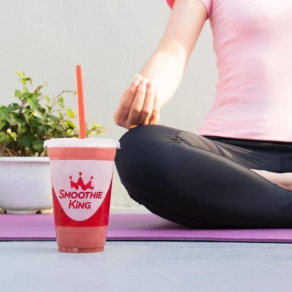 A woman savoring a smoothie on a yoga mat embodies the connection between smoothies and the health and wellness industry.