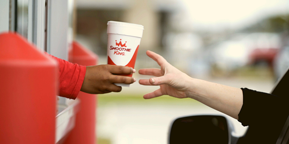 A person delivering exceptional guest service by handing someone a cup of Smoothie King.