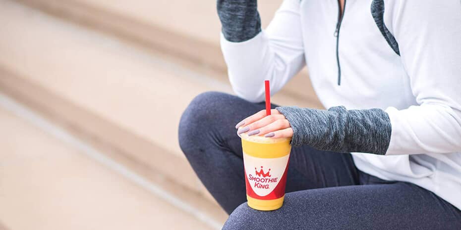 A woman is sipping a drink on steps as a Smoothie King Franchisee.
