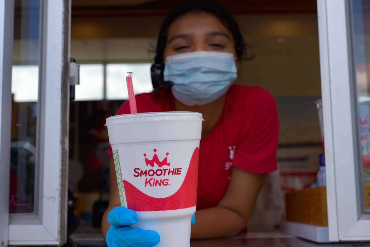 A woman, masked and gloved, serves a cup of ice cream at a drive-thru smoothie concept.