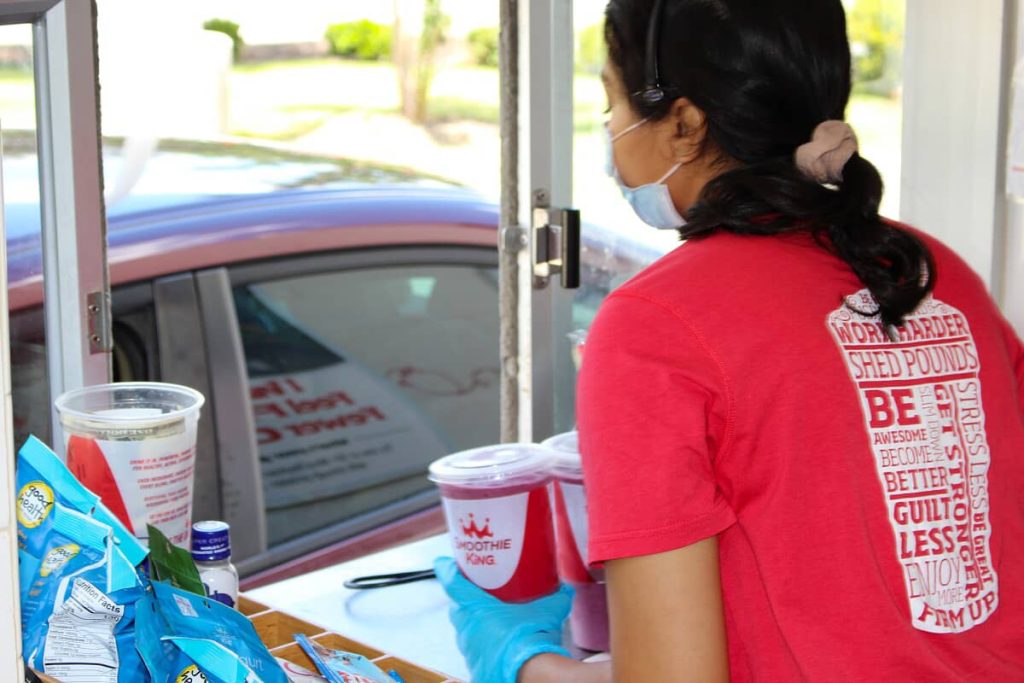 A woman in a red Smoothie King shirt is standing in front of a drive-thru smoothie concept.