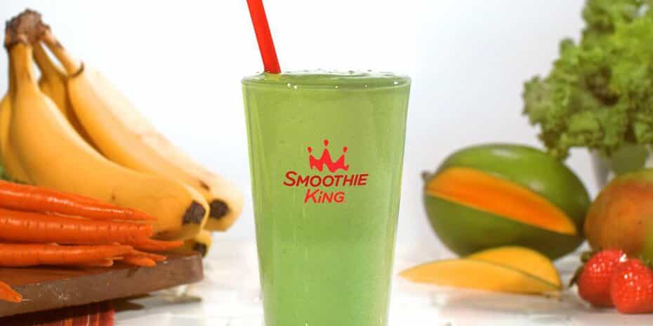 The Franchisee behind Smoothie King’s Vegan Smoothie Line introduces a green smoothie with a red straw amidst fruits and vegetables.