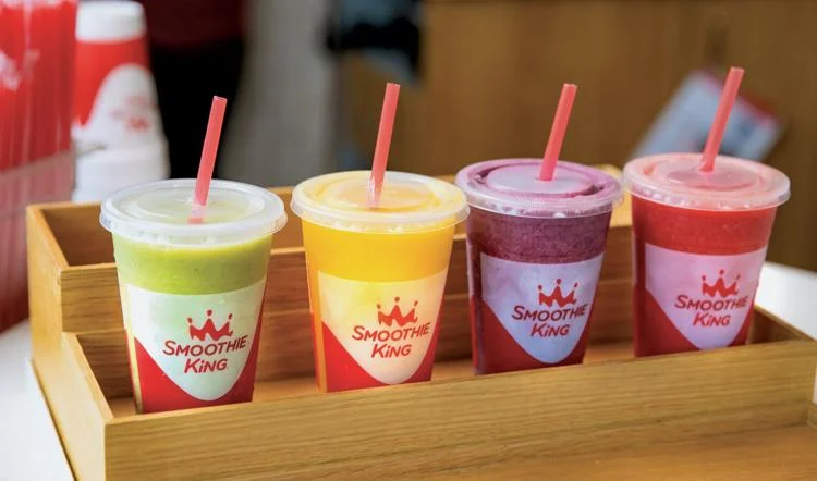 Four cups of smoothies are lined up on a wooden tray at a smoothie bar franchise.